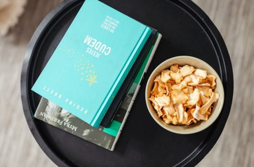 Aerial view of a stack of books and a snack bowl on a round table, creating a cozy reading nook.